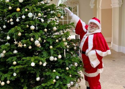 Mighty Fozzy Santa Claus hanging a bauble on the christmas tree at Old Down Country Park